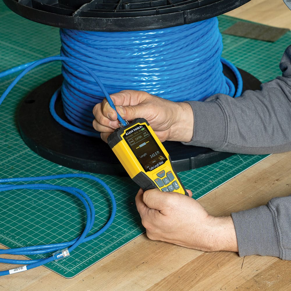 Action shot demonstrating a direct connection to a bulk spool of CAT6A data cable using the 501915 TDR meter. The technician is shown plugging a terminated Ethernet cable directly into the meter's RJ45 port to verify the total length of 343.0 feet remaining on the industrial spool.