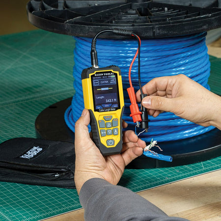Action shot of the 501915 cable meter measuring an unterminated spool of blue CAT6A data cable. The image highlights the use of the professional alligator clip adapters to interface with the individual twisted pairs, providing an accurate length reading of 343.1 feet for inventory verification.