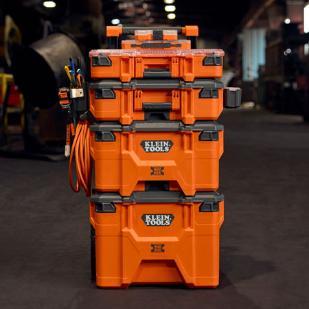 Front profile view of a complete Klein Tools MODbox modular tool stack inside a workshop, featuring the rolling base, two medium boxes, and a small parts organizer with side rail accessories.