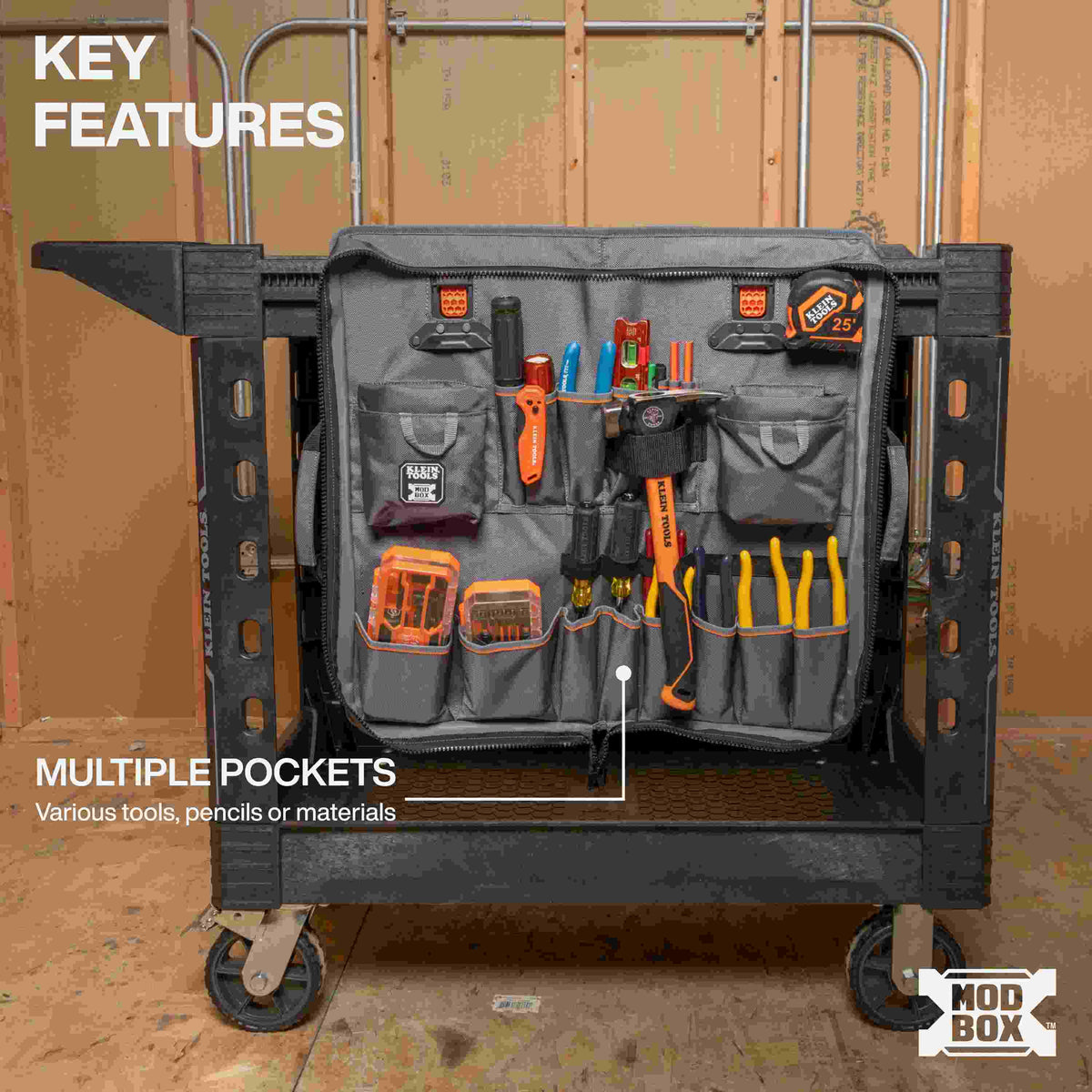 A MODbox Tool Apron attached to the side of a utility cart, fully loaded with various tools including a hammer, screwdrivers, pliers, a tape measure, and hardware bins. A caption points to the multiple pockets designed for various tools, pencils, or materials.