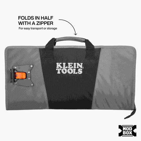 The MODbox Tool Apron shown zipped shut and folded in half for transport. It features a sturdy gray carrying handle and a large Klein Tools logo on the front. A caption notes that it folds in half with a zipper for easy transport or storage.