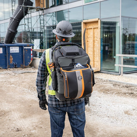 An action lifestyle shot showing a professional ironworker wearing the 55665 backpack on a construction site. The bag is shown carrying a large 36-inch connecting bar and a hard hat, demonstrating its specialized storage capacity for structural steel workers.