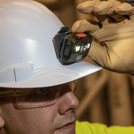 A close-up view of a technician using a gloved hand to pivot the headlamp while it is mounted on a hard hat, demonstrating the adjustable 160-degree lighting angle.