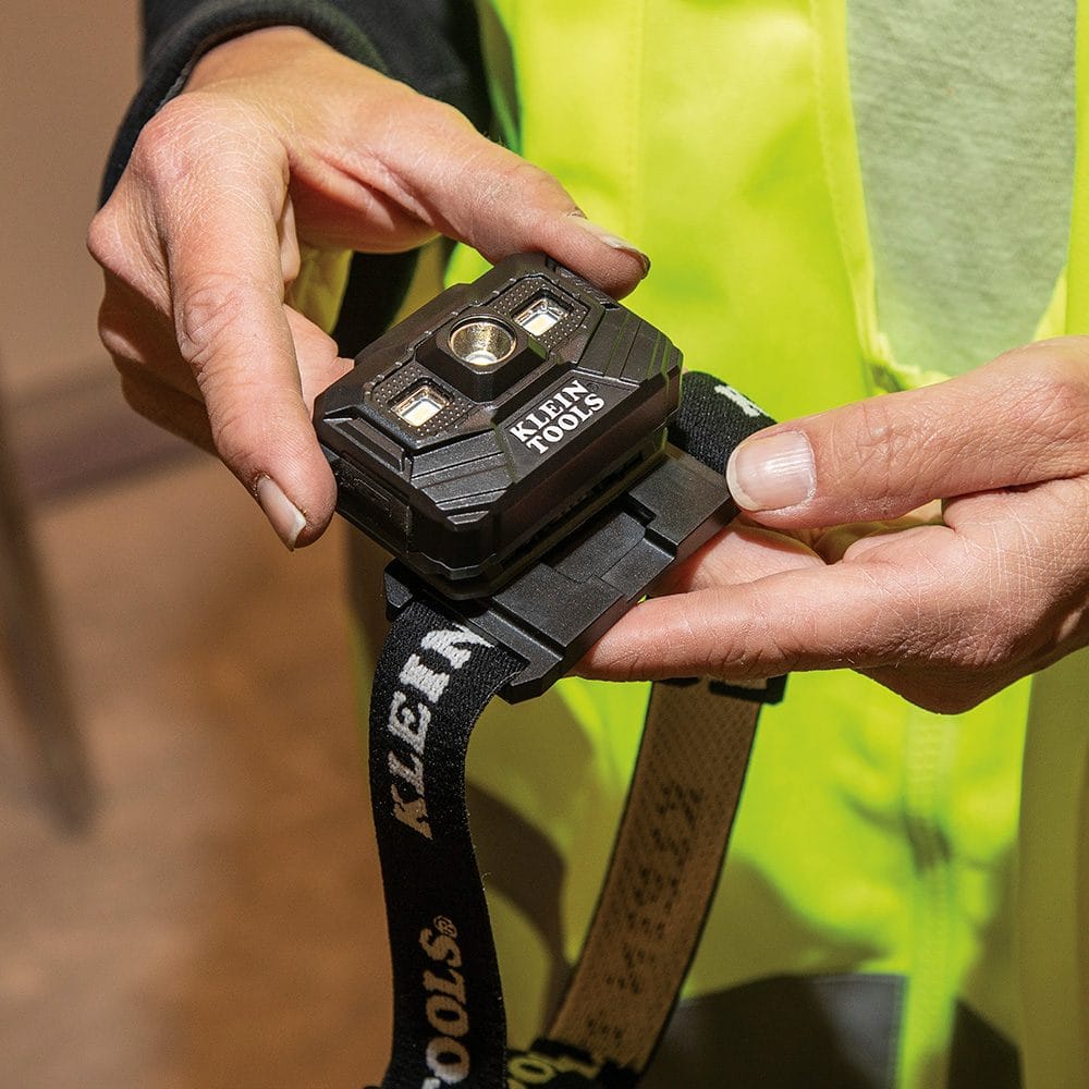 A person holding a black fabric headband with a mounting bracket, showing how the headlamp can be attached to a strap for use without a hard hat.