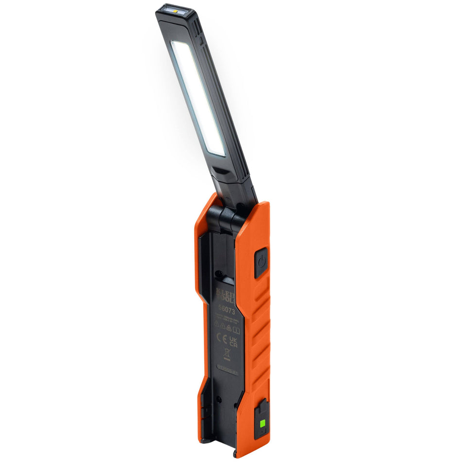 A professional product view of the Klein Tools 56073 rechargeable LED work light in its unfolded position, featuring a rugged orange and black housing and a slim, high-output foldable lighting arm.