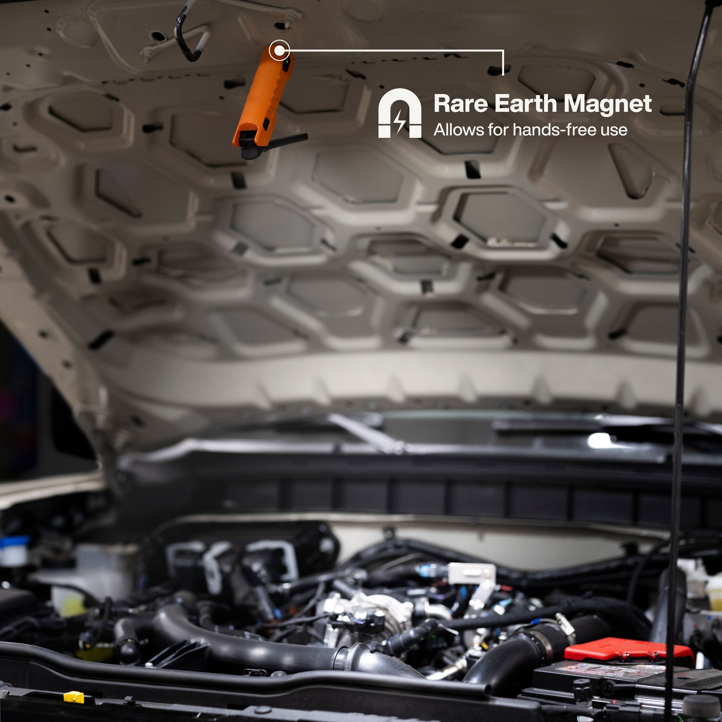 The orange foldable work light secured to the underside of a vehicle hood using its powerful N50 rare-earth magnetic base, illustrating hands-free use for automotive repair and maintenance.