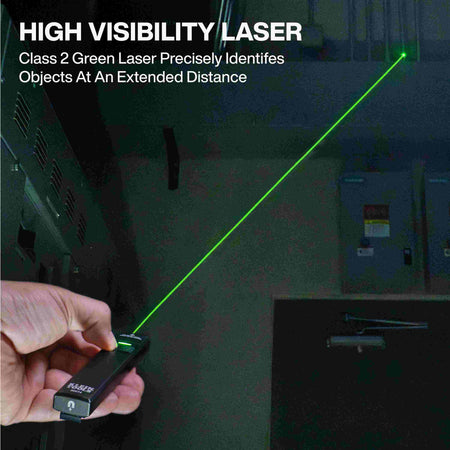 A first-person perspective of a hand holding the flashlight and pointing the bright green Class 2 laser beam at distant overhead ductwork in a dark room.