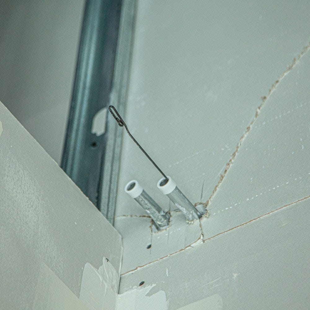 View of the steel fish tape hook emerging from a metal conduit pipe installed in a drywall frame.