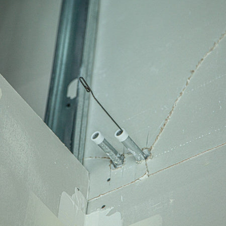 View of the steel fish tape hook emerging from a metal conduit pipe installed in a drywall frame.