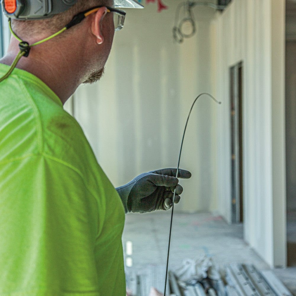 A worker in a green shirt holding a length of the steel fish tape to demonstrate its flexibility and stiffness.