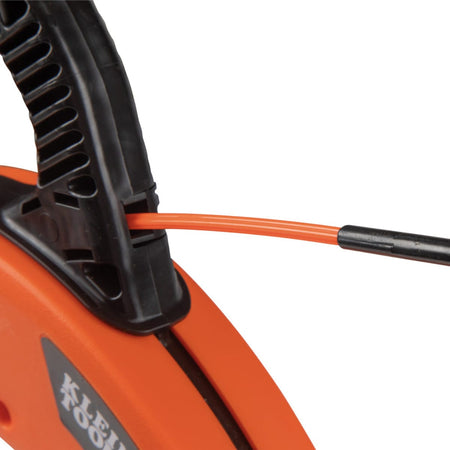 Macro view of the fish tape payout port, showing the orange multi-groove fiberglass tape as it exits the slip-resistant housing for a controlled and effortless wire pulling experience.