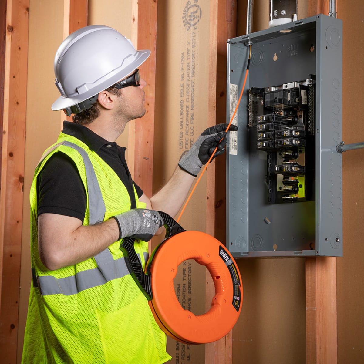 A professional electrician feeding the Klein Tools 56380 fiberglass fish tape into an electrical panel, demonstrating its effective use in commercial wire pulling and data installation projects.