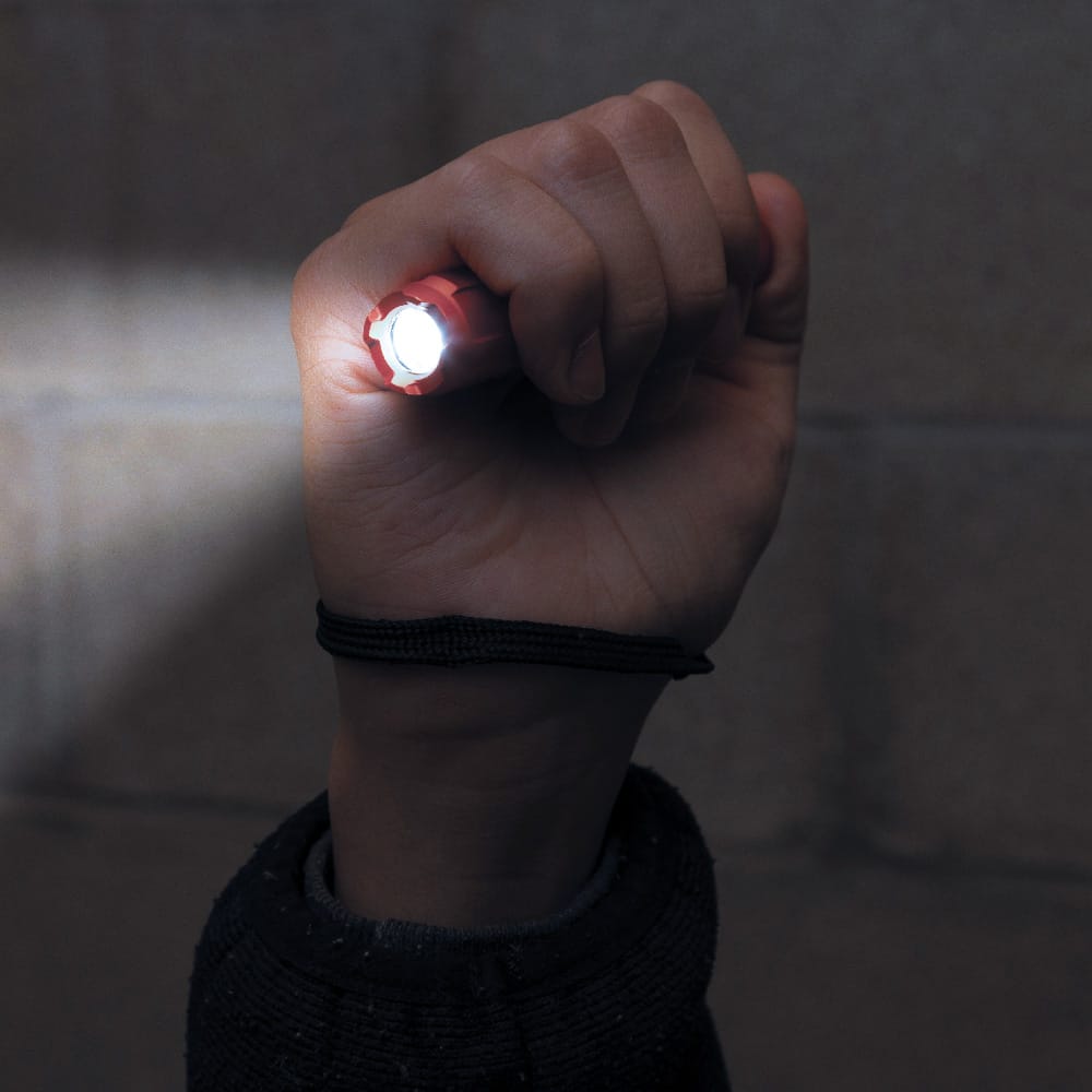 A functional demonstration of the flashlight being held in a fist, showing the powerful 275-lumen LED beam illuminating a workspace while the safety lanyard is securely looped around the user's wrist.