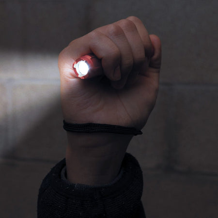 A functional demonstration of the flashlight being held in a fist, showing the powerful 275-lumen LED beam illuminating a workspace while the safety lanyard is securely looped around the user's wrist.