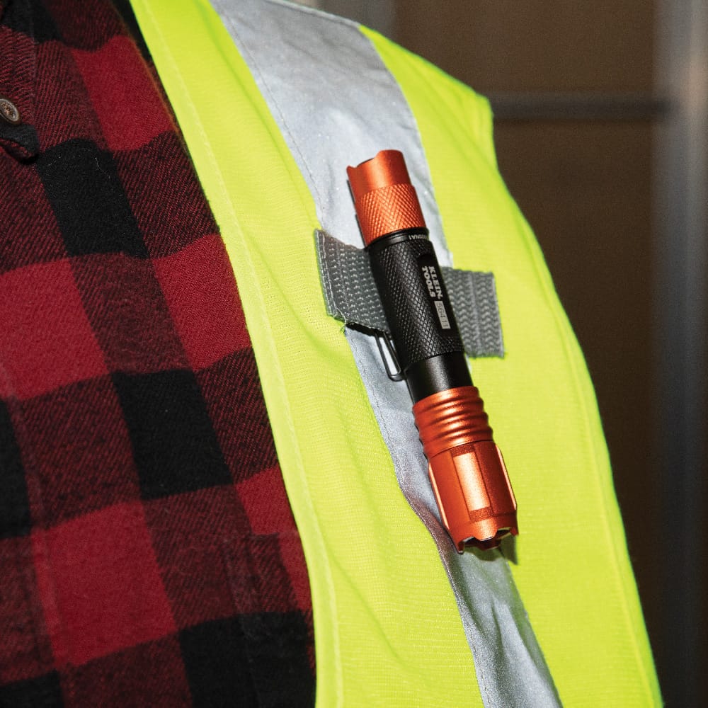 The waterproof pocket light shown clipped to the shoulder strap of a high-visibility safety vest over a red flannel shirt, highlighting the versatile carry options and compact design for easy access on the job.