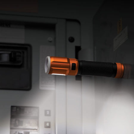 Klein Tools 56412 flashlight mounted horizontally to a metal electrical panel using its magnetic cap, utilizing the side-barrel LED work light for hands-free job site illumination.