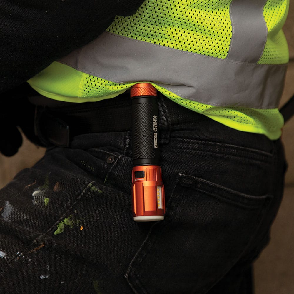 Worker wearing a high-visibility safety vest carrying the Klein Tools 56412 drop safe daily job site gear flashlight securely attached to their front pocket using the removable pocket clip.