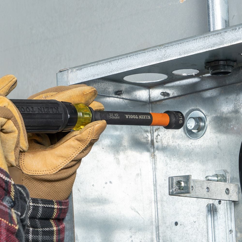 A close-up of a gloved hand using the nut setter to fasten a bolt inside a metal electrical junction box.