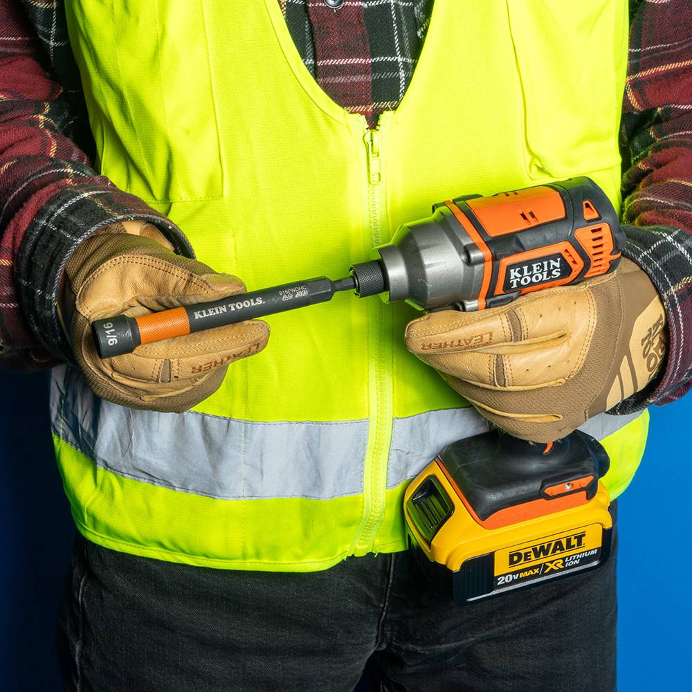 A worker's hand holding the impact driver with the nut setter attached, demonstrating the magnetic holding power by keeping a large bolt secure upside down.