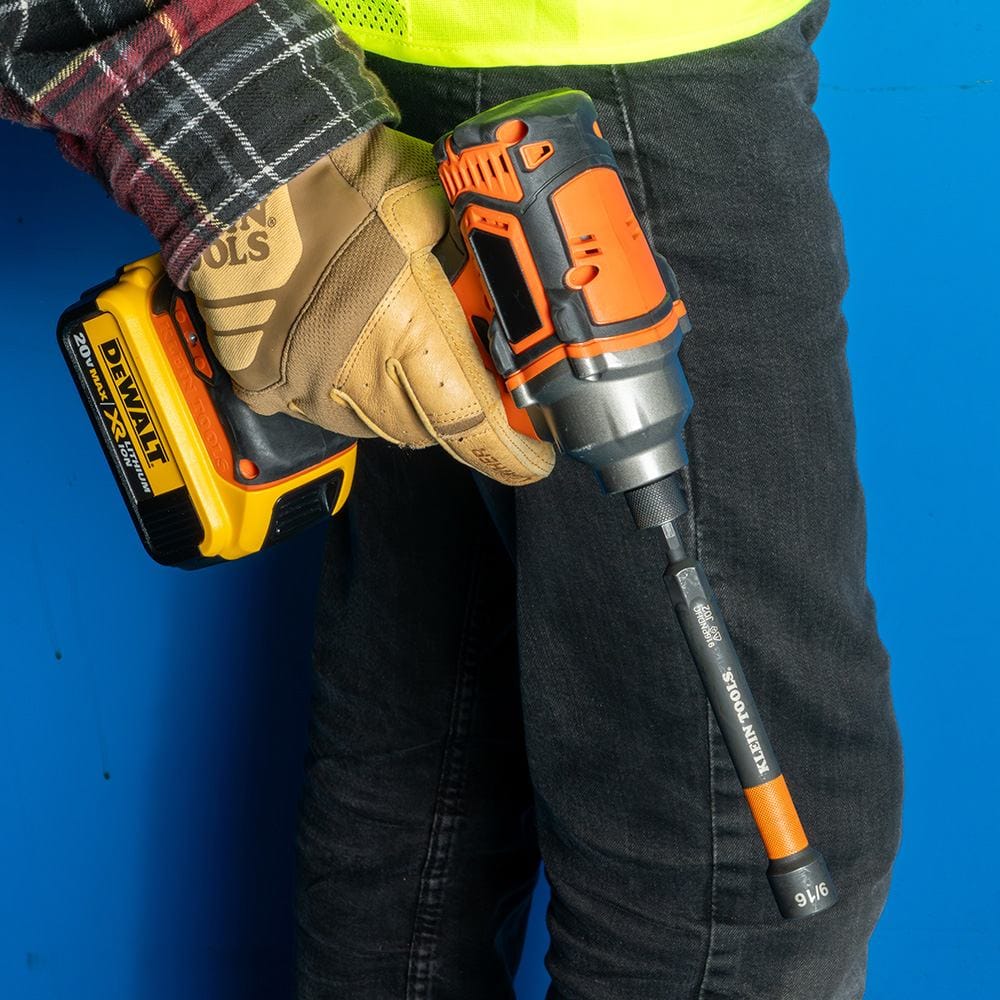 A worker using an impact driver with the orange-banded nut setter to drive a fastener into a wall, showcasing the extended reach.