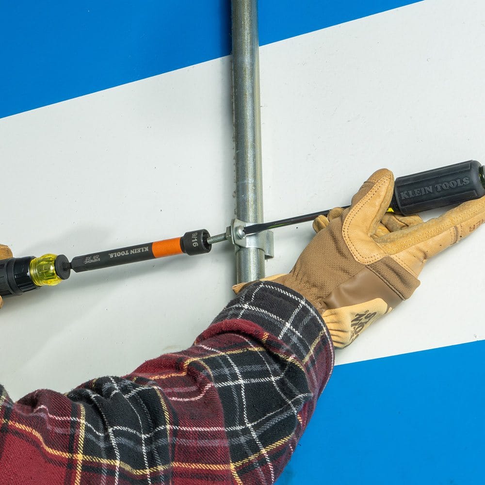 A close-up view of the orange 9/16 inch nut setter being used to tighten a nut on a conduit clamp attached to a vertical pipe.