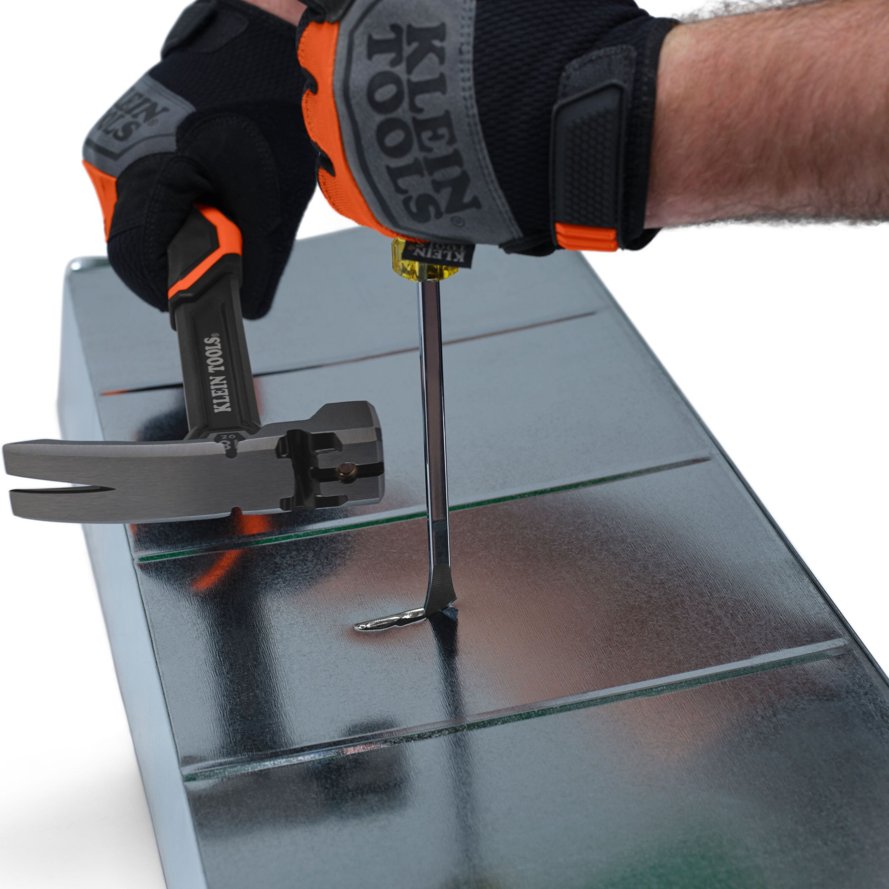 Action shot of a professional wearing Klein Tools safety gloves using a hammer to strike the demolition driver to slit a section of galvanized metal ductwork.