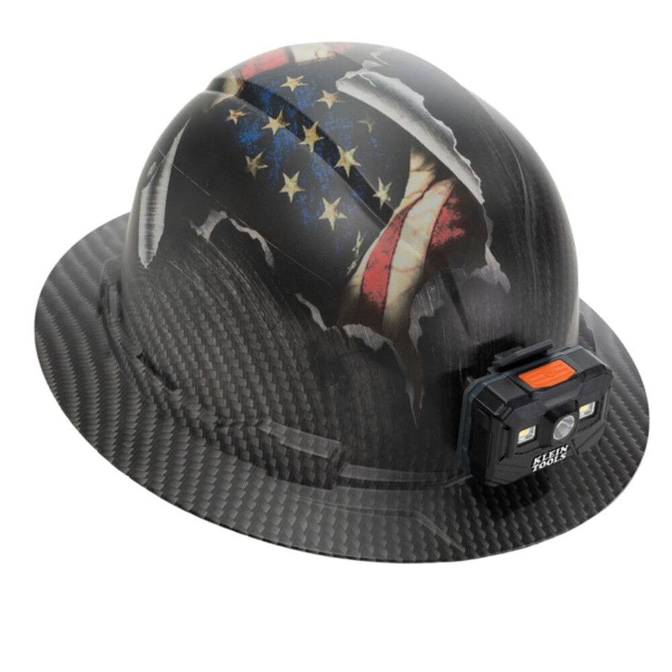 Perspective view of the Klein Tools 60346FS full brim hard hat featuring a hydro-dipped KARBN pattern and American flag graphic with a front-mounted rechargeable LED headlamp.
