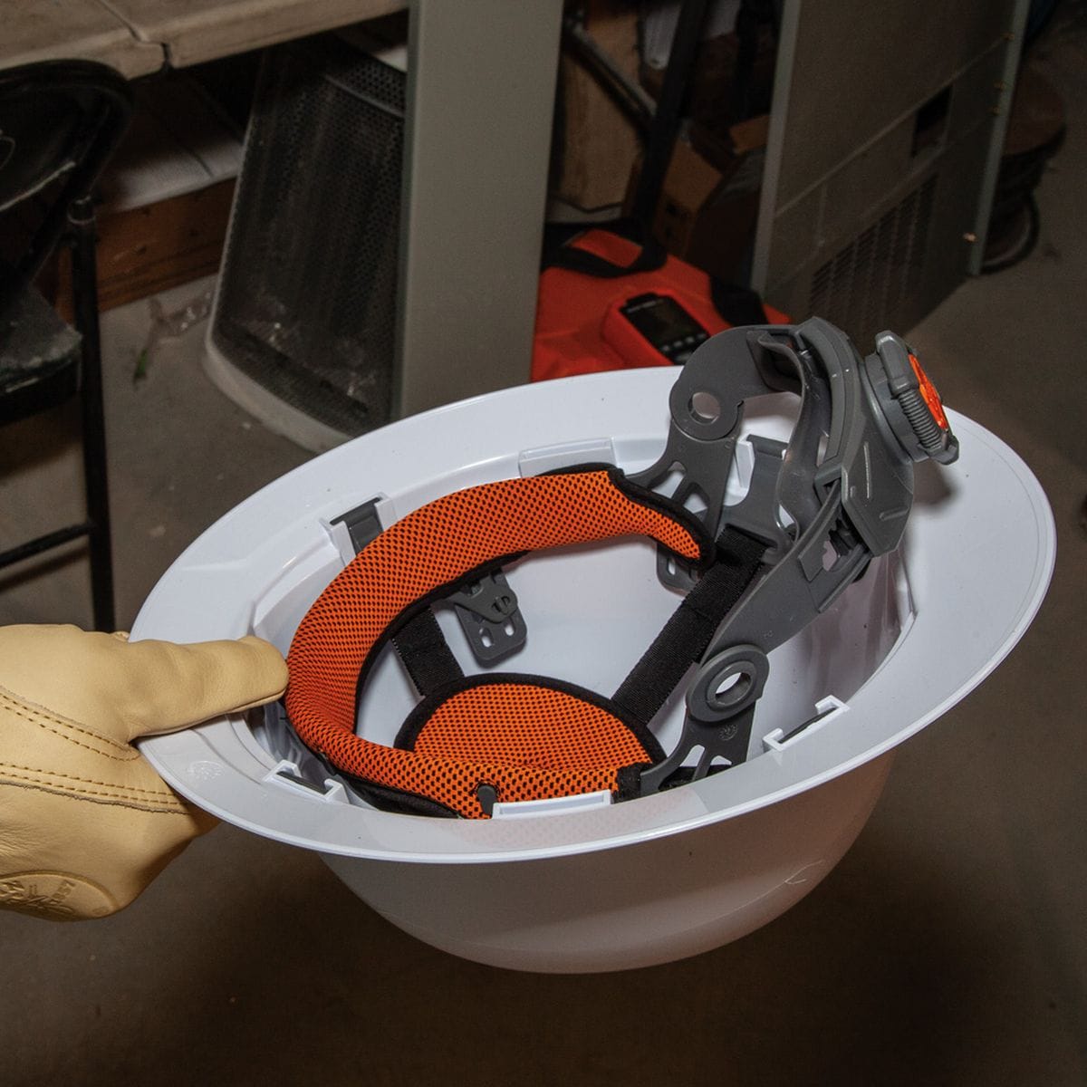 An interior perspective of the hard hat being held by a gloved hand, showcasing the 4-point suspension system and the orange, padded, sweat-wicking sweatband.