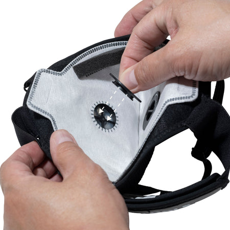 An operational view demonstrating the final step in replacing the N95 filter, with hands aligning and pressing the circular central mask valve into the precise port opening of the white Klein Tools replacement filter.