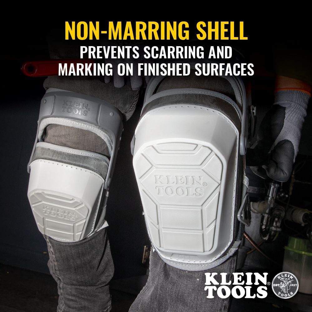 Action shot of a professional wearing the Klein Tools 60897 knee pads while kneeling in a dark work area. The white non-marring shells are featured prominently, preventing scarring and marking on finished floor surfaces.