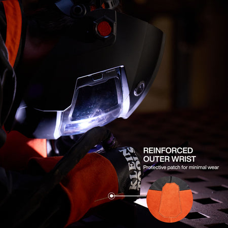 An action lifestyle shot focusing on the reinforced outer wrist of the Klein Tools welding glove. A circular detail zoom shows the protective patch engineered for minimal wear in high-friction areas while the technician performs a precision TIG weld.