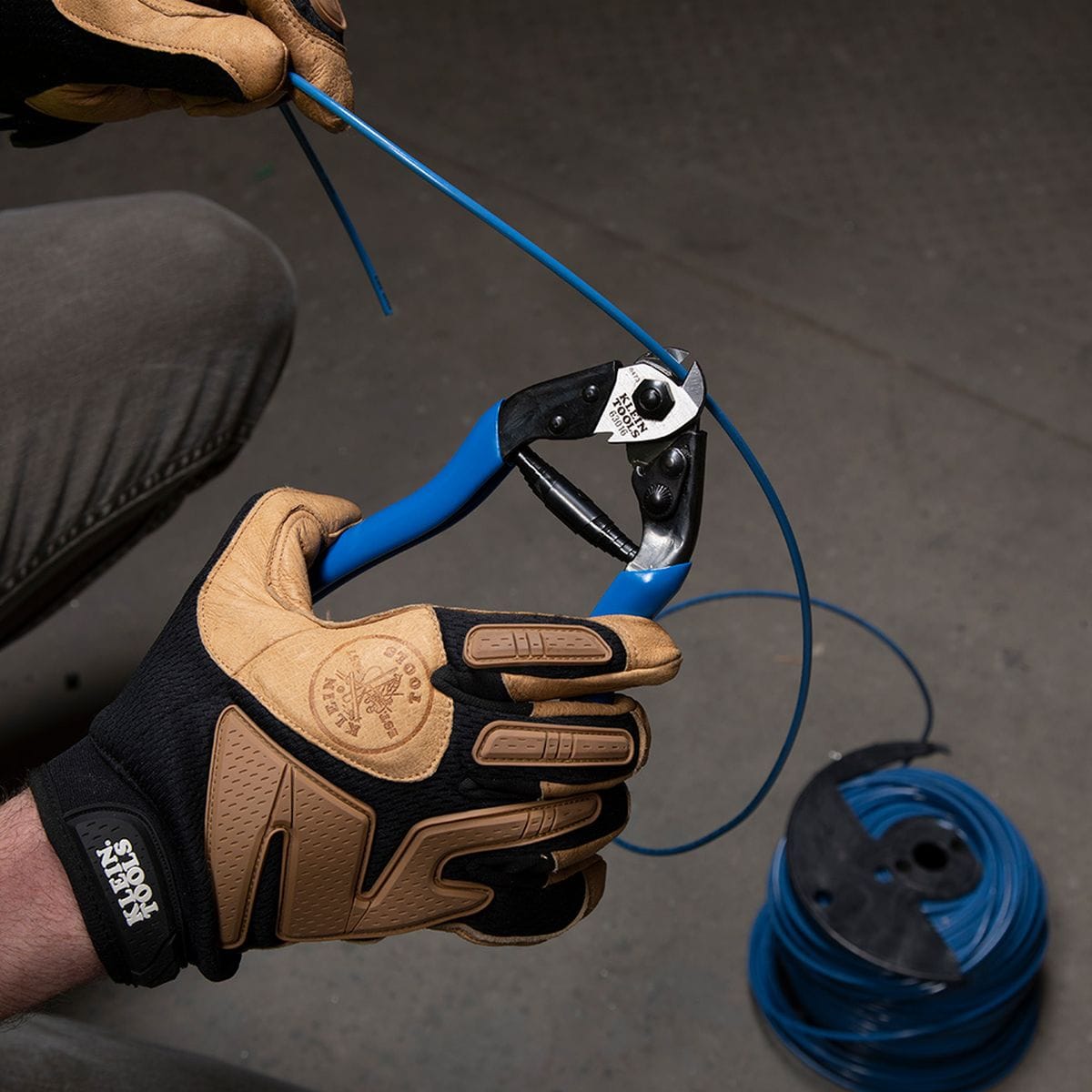 An application photo showing the 63016 shears performing a clinical cut on a blue insulated conductor, demonstrating the tool's versatility for both soft metals and hardened reinforced cables.