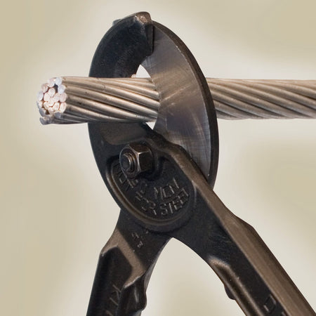 A detailed macro shot showing the shear-type cutting action of the Klein Tools cable cutter as it slices through a large-diameter aluminum cable, demonstrating the precision-ground blades and the 500 MCM Copper and 750 MCM Aluminum maximum capacity.