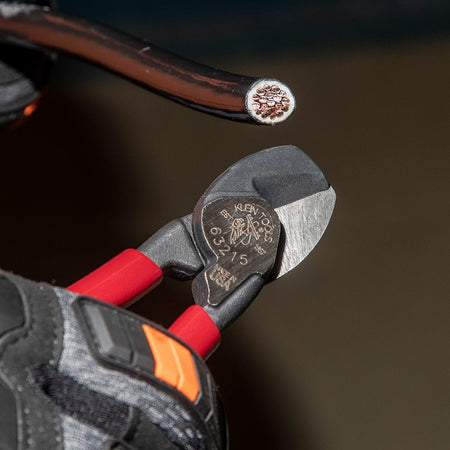 A detailed application photo showing the precision-ground shear blades of the 63215 compact cutter as they sever a small insulated conductor, highlighting the clinical accuracy and burr-free finish.