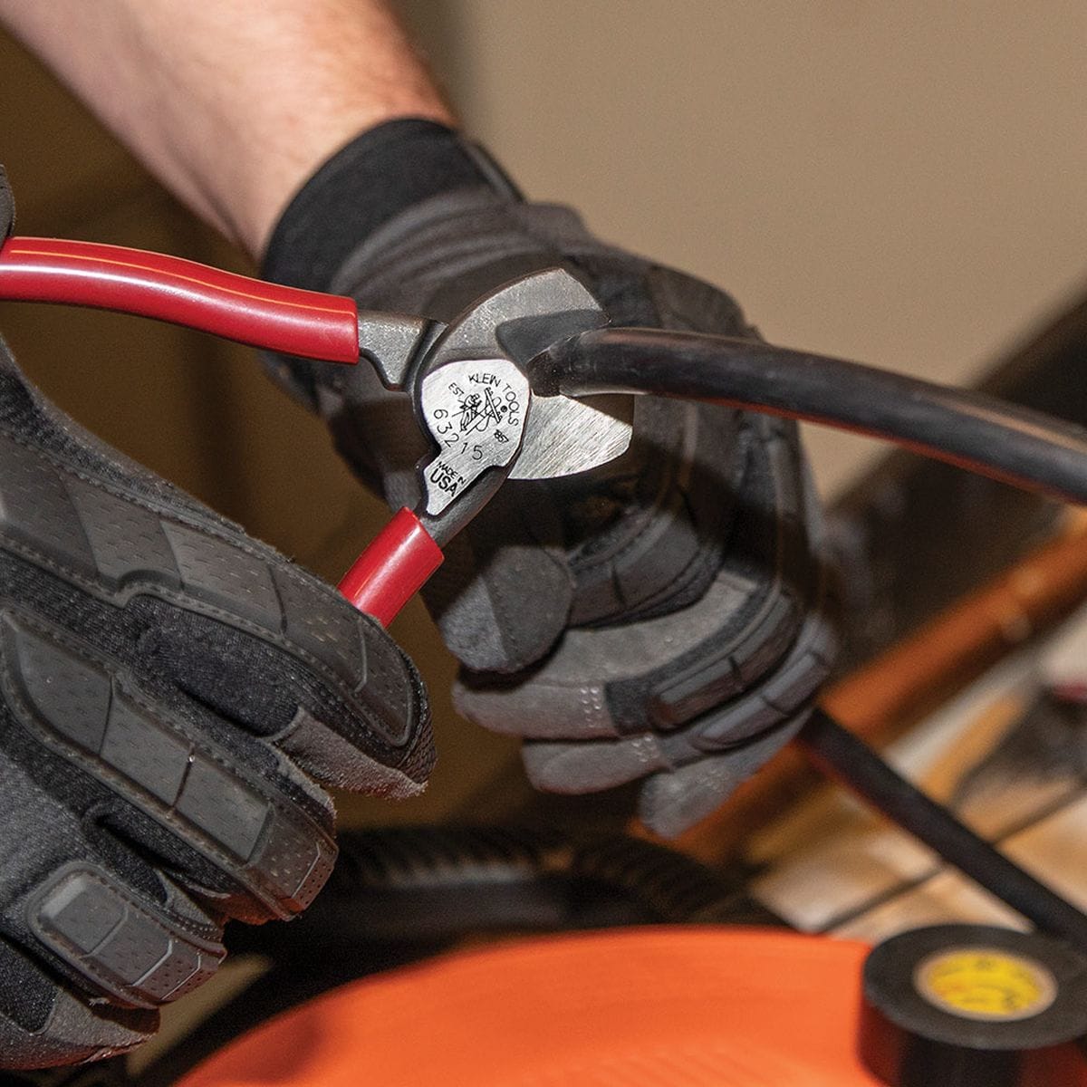 An application photo of a professional in safety gloves using the 63215 compact cutter to perform a clean shear cut on a black insulated conductor, demonstrating its one-handed mechanical advantage.