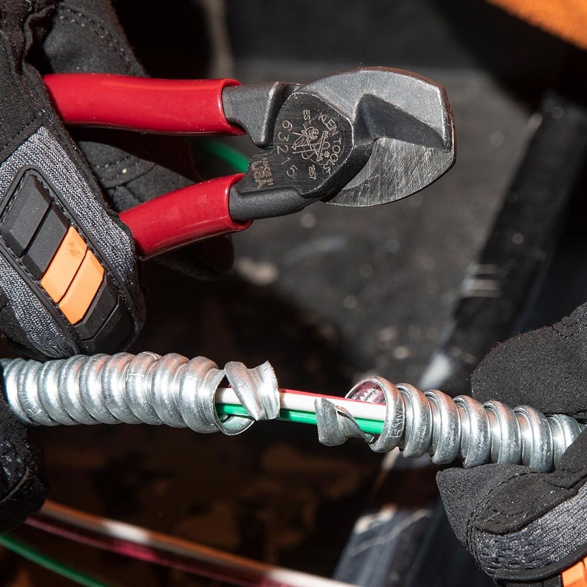A detailed application shot showing the 63215 high-leverage cutter being used to score and remove the aluminum jacket from a piece of Metal Clad (MC) cable, revealing the internal insulated wires.