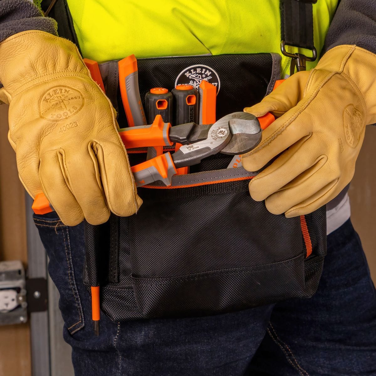 A lifestyle shot showing the 63225RINS insulated cable cutter being placed into a professional tool pouch alongside other electrical hand tools, demonstrating its portability for field work.