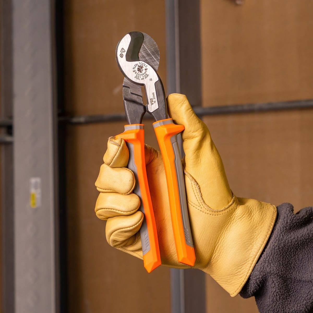 A detail shot of a gloved hand holding the 63225RINS insulated high-leverage cable cutter, emphasizing the secure-grip handles and the specialized jaw geometry optimized for 4/0 aluminum and 2/0 soft copper.