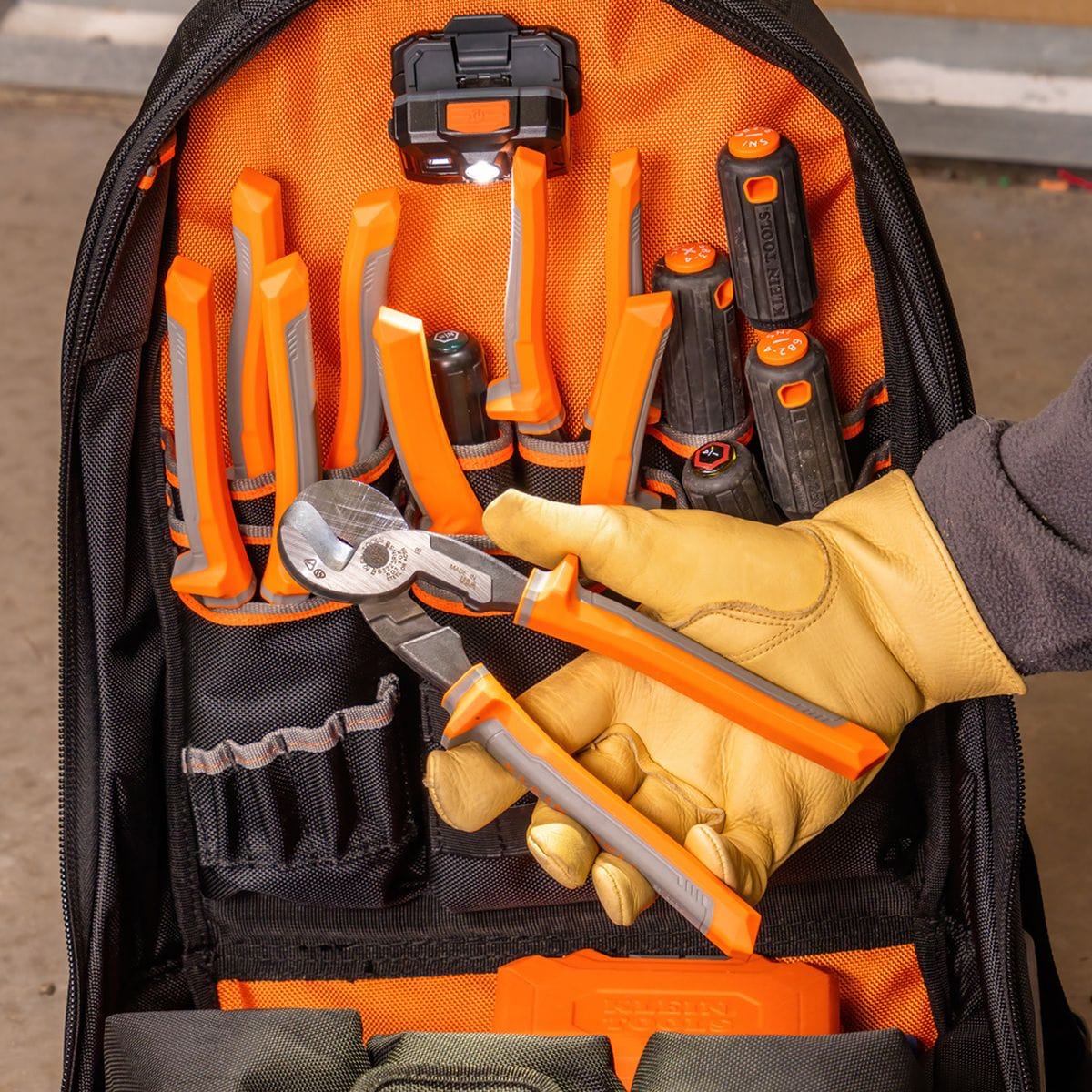 A professional view of a tradesperson organizing the 63225RINS insulated cable cutter into a specialized orange and black tool backpack, showcasing its compact size for industrial mobile maintenance.