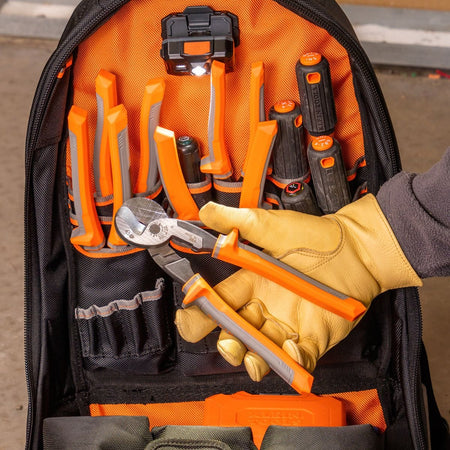 A professional view of a tradesperson organizing the 63225RINS insulated cable cutter into a specialized orange and black tool backpack, showcasing its compact size for industrial mobile maintenance.