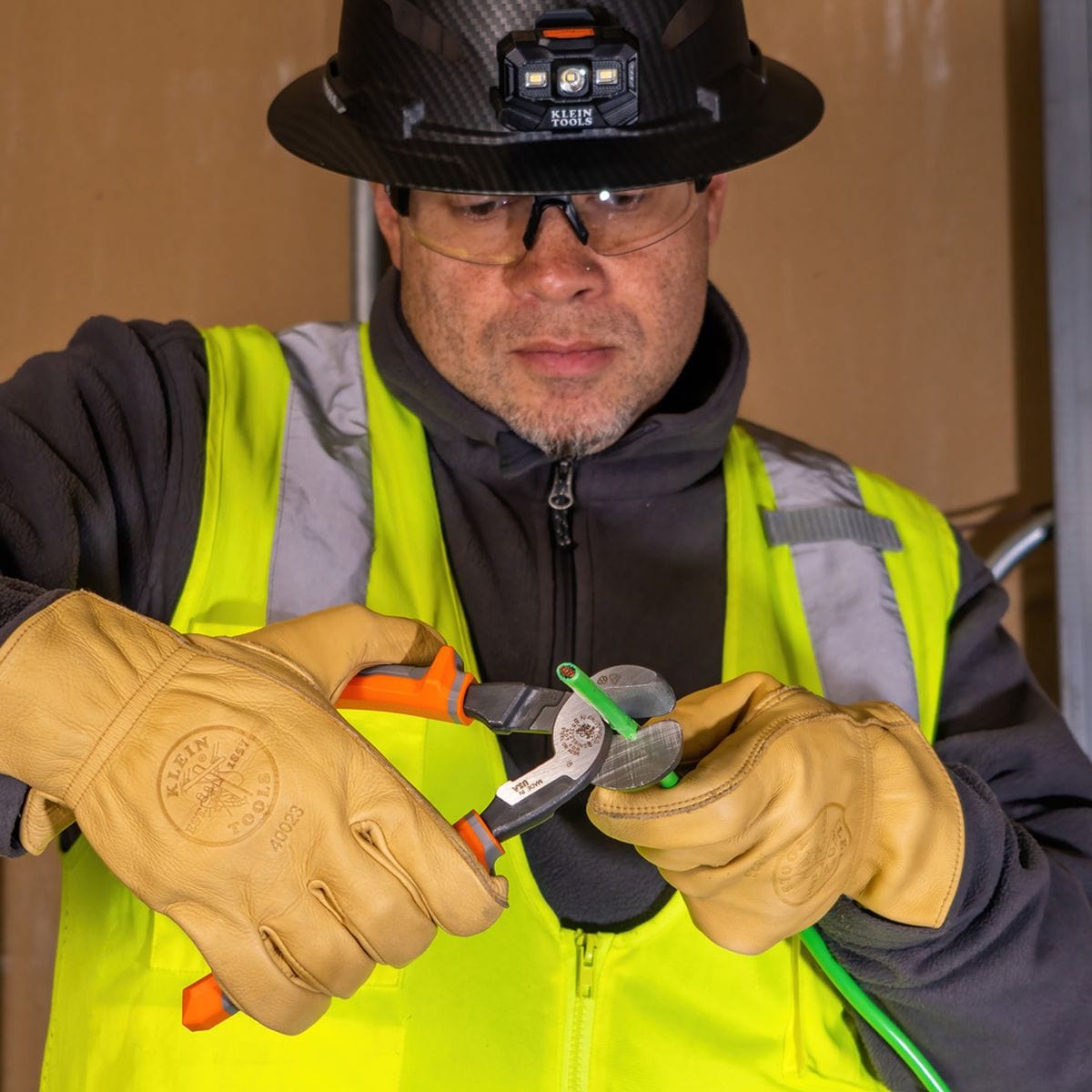 A jobsite photo of a professional electrician in full safety gear utilizing the 1000V insulated high-leverage cutter to perform a clean, precision shear cut on a conductor.