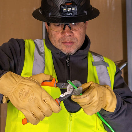 A jobsite photo of a professional electrician in full safety gear utilizing the 1000V insulated high-leverage cutter to perform a clean, precision shear cut on a conductor.
