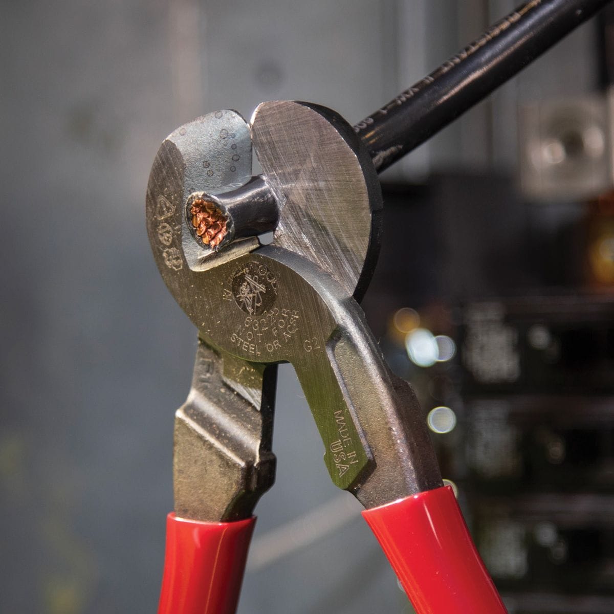 An action shot of the 63225 cable cutter performing a clean, burr-free shear cut on a black insulated conductor inside an electrical panel, demonstrating its efficiency in tight service enclosures.