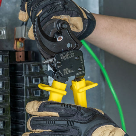 An application photo showing the 63607 ratcheting cutter engaging a large-diameter aluminum conductor, demonstrating the tool's specialized jaw geometry for non-compression shearing.