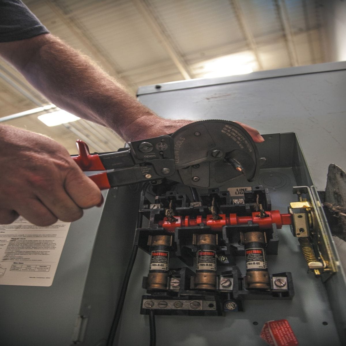 A jobsite photo of an electrician utilizing the single-handed ratcheting action of the 63711 to cut cable inside a fused disconnect switch, highlighting the front-loading jaw's efficiency in tight electrical enclosures.