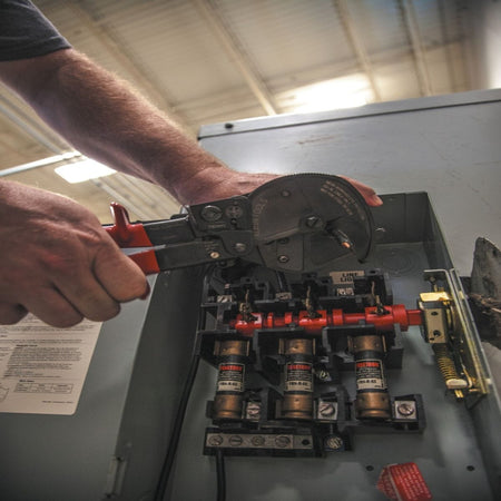 A jobsite photo of an electrician utilizing the single-handed ratcheting action of the 63711 to cut cable inside a fused disconnect switch, highlighting the front-loading jaw's efficiency in tight electrical enclosures.