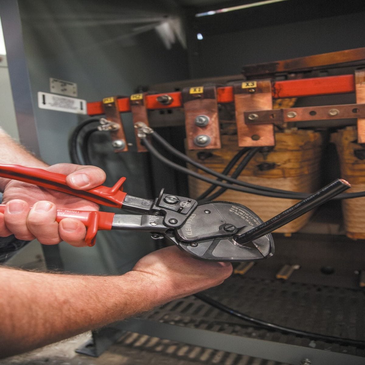 An action shot of a professional tradesperson using the 63711 open-jaw cutter to shear a large copper conductor inside an industrial electrical cabinet, demonstrating the tool's tactical advantage in confined service areas.