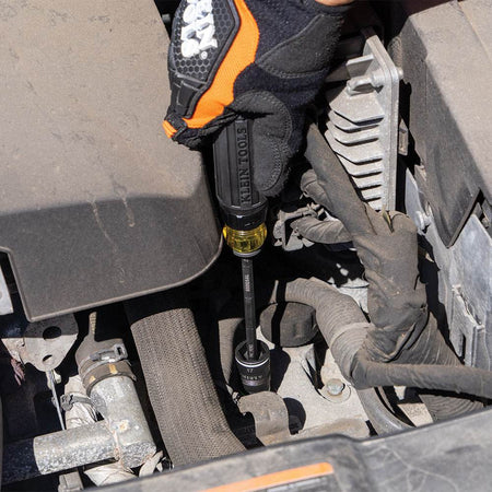 A close-up view of the Klein Tools ratcheting handle and 17 mm flip socket reaching a deep-seated fastener in a crowded engine compartment, highlighting the tool's ability to provide high-torque impact-rated driving in tight spaces.