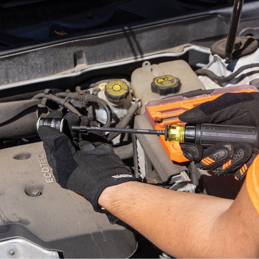 A professional tradesperson in work gloves attaching a color-coded flip socket to the long KNECT adapter. The image showcases the quick-connect functionality of the system for efficient transitions between different fastener sizes under a car hood.
