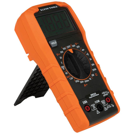 Angled perspective of the Klein Tools MM320 multimeter with the integrated kickstand extended. The view showcases the ergonomic orange holster and the large dial used to select between voltage, resistance, and current measurement modes.